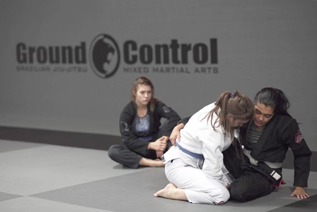 Two women grappling on the ground in a martial arts facility