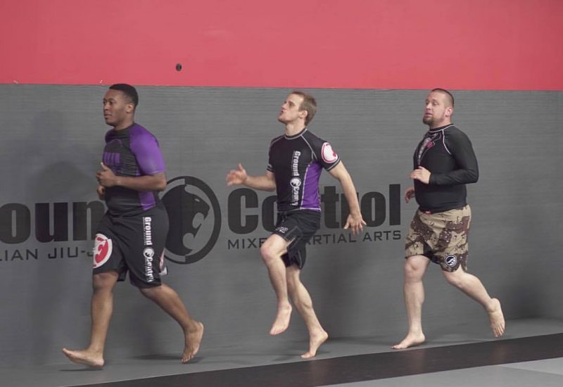 Three men jogging around a mat in a conditioning class