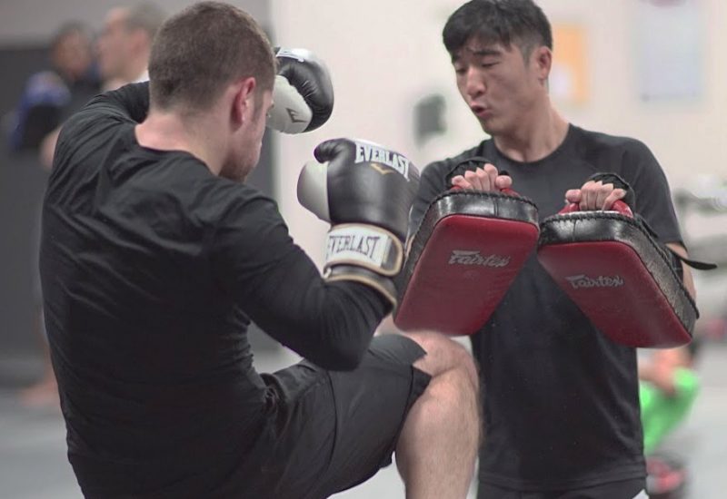 Man practicing muay thai with another man holding strike pads